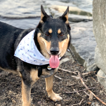 Black and brown German Shepherd with tongue out wearing a white bandana with dark blue illustrations.